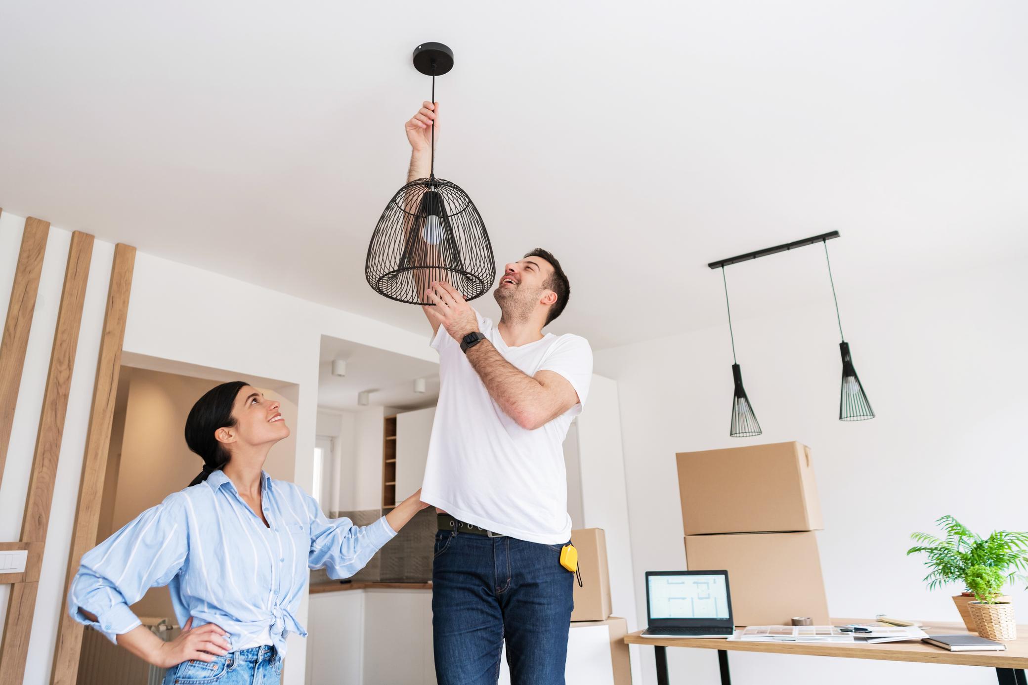 Junges Paar hängt Lampe im Wohnzimmer auf