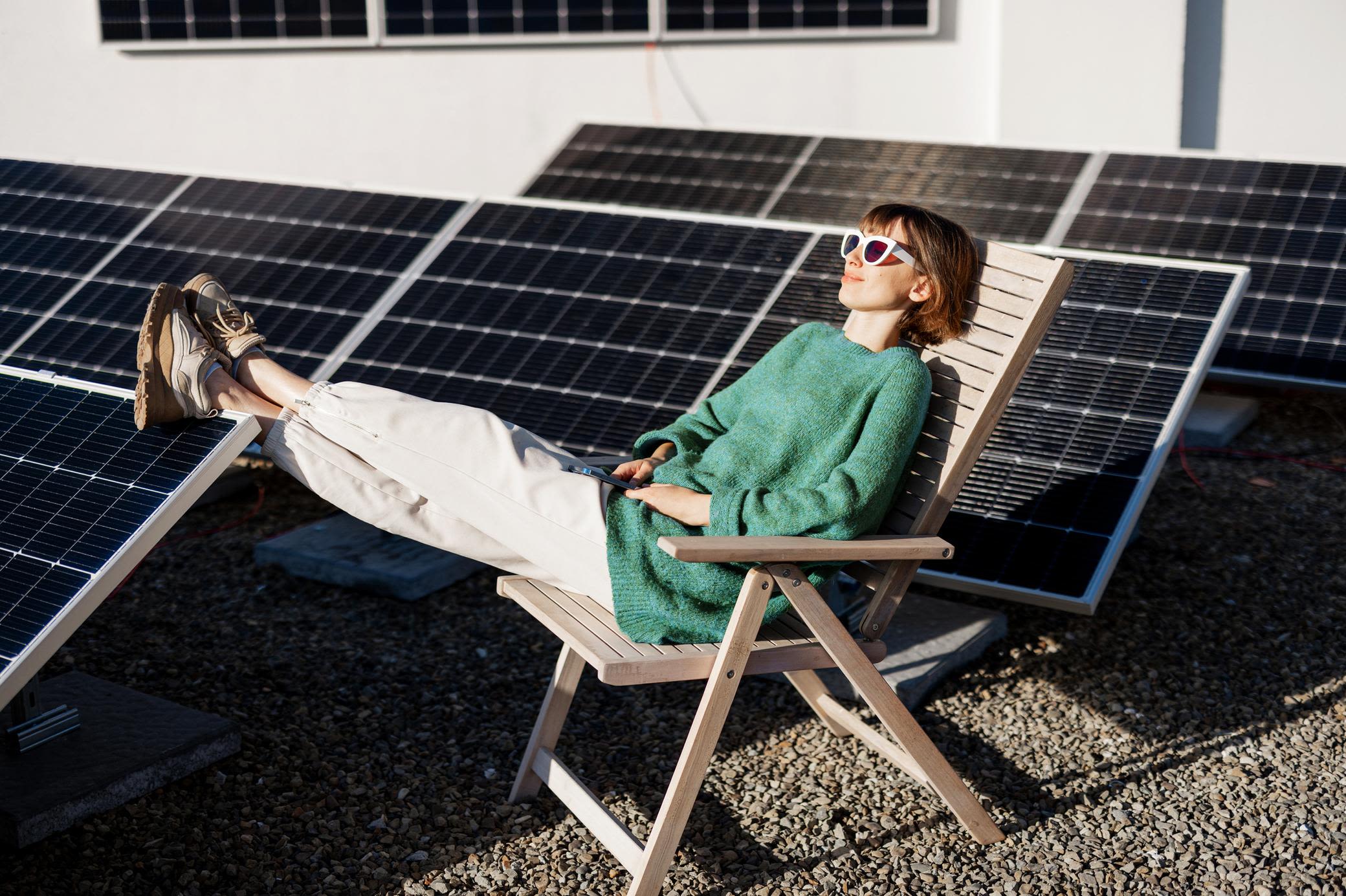 Solaranlagen gibt es auch für dein Flachdach Frau liegt entspannt auf einem Holzstuhl auf einem Flachdach mit Solaranlage
