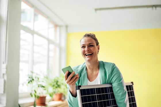 Mach's dir einfach mit Yello Hub und sieh deine Solarerzeugung Eine lachende Frau die ein Handy in der Hand hält und ein kleines Solarmodul hält