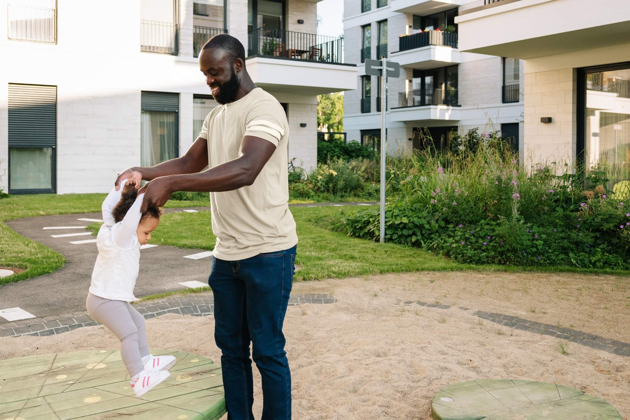 Mann spielt mit Kleinkind auf einem Spielplatz im Mehrfamilienhaus