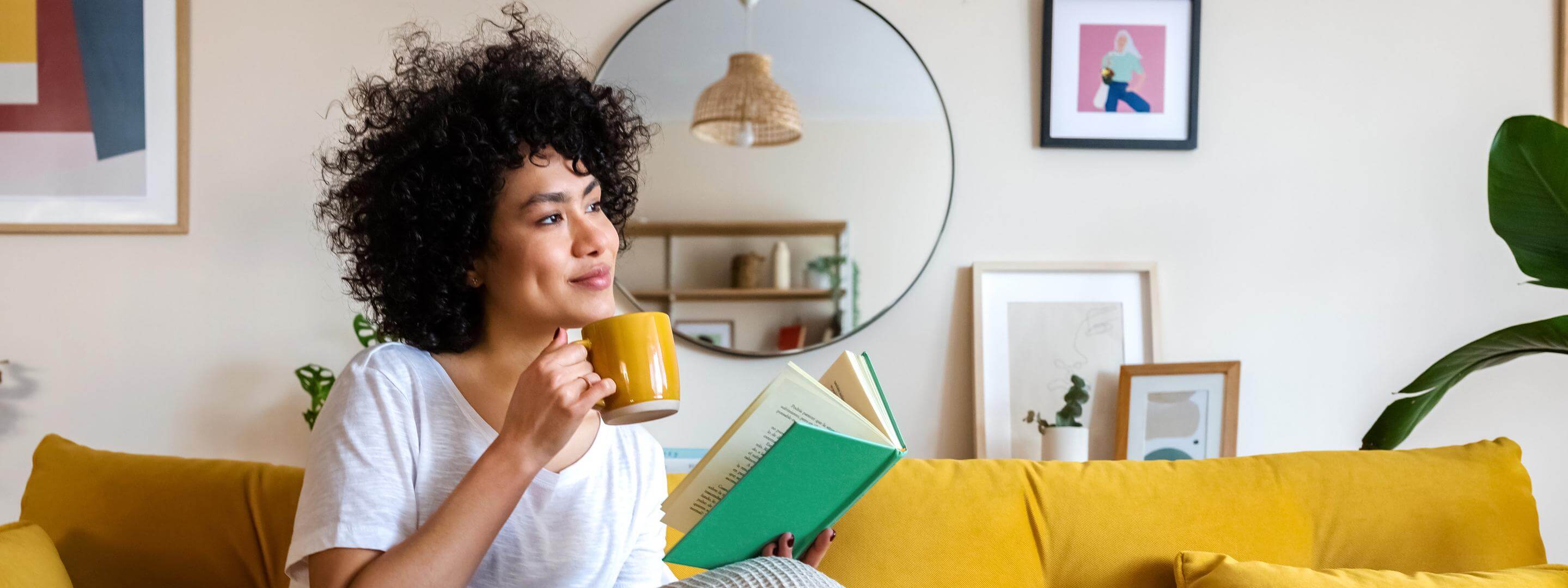 So geht Wärmedämmung richtig! Junge Frau sitzt auf dem Sofa und liest ein Buch mit einer Tasse in der Hand.