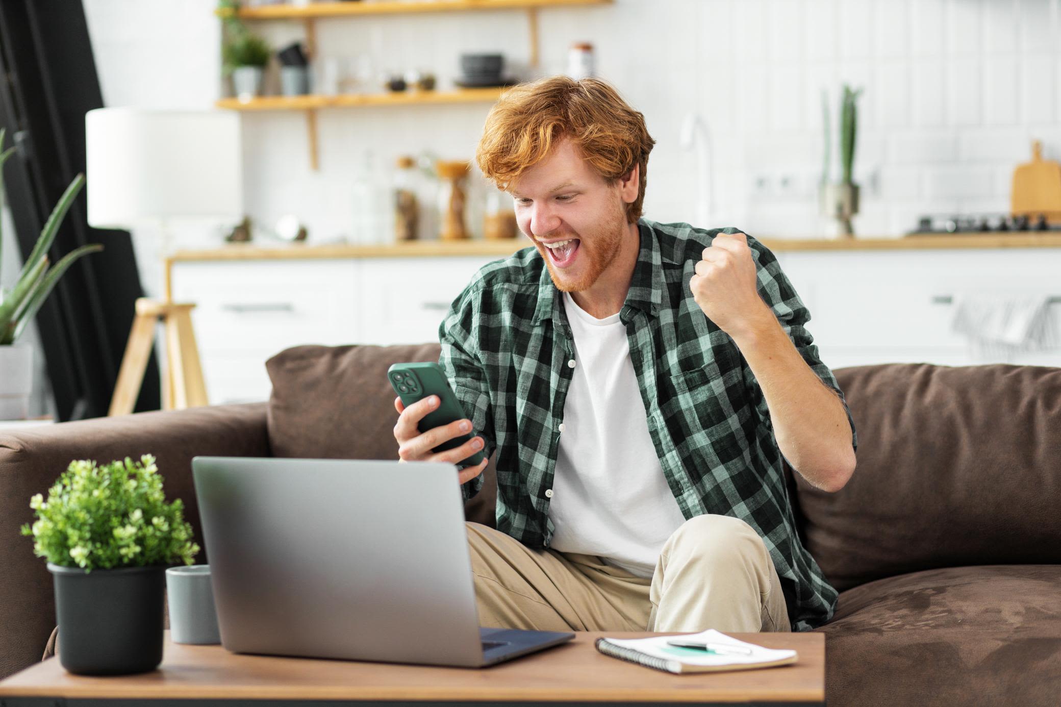 Datensicherheit spielt im Energiemarkt eine wichtige Rolle Jubelnder Mann im Homeoffice mit Laptop und Handy