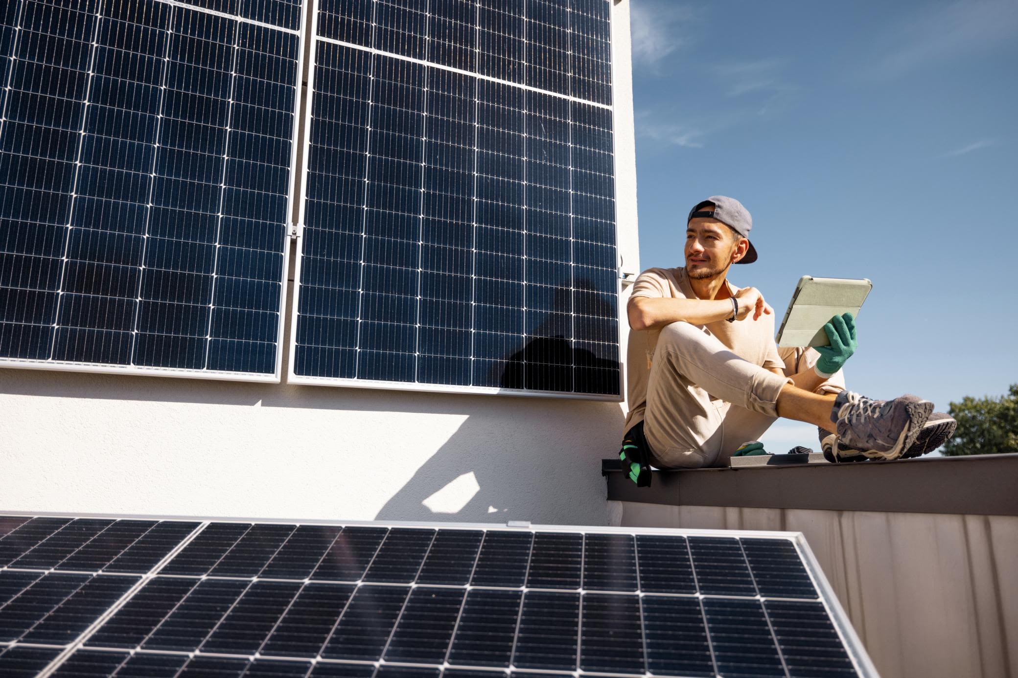 Eine PV-Anlage versorgt dich zuverlässig mit eigenem Strom Mann prüft Solarmodule auf einem Dach mit Tablet