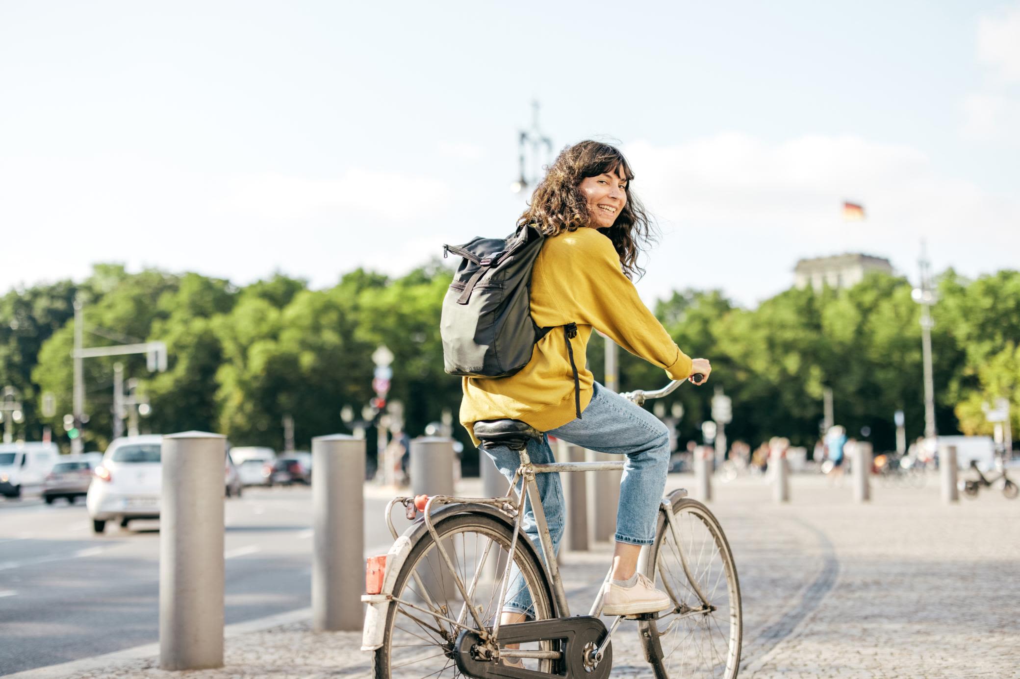 Stromtarife in Berlin - Mit Yello als fairem Stromanbieter Frau mit Fahrrad in Berlin fährt in Richtung Brandenburger Tor