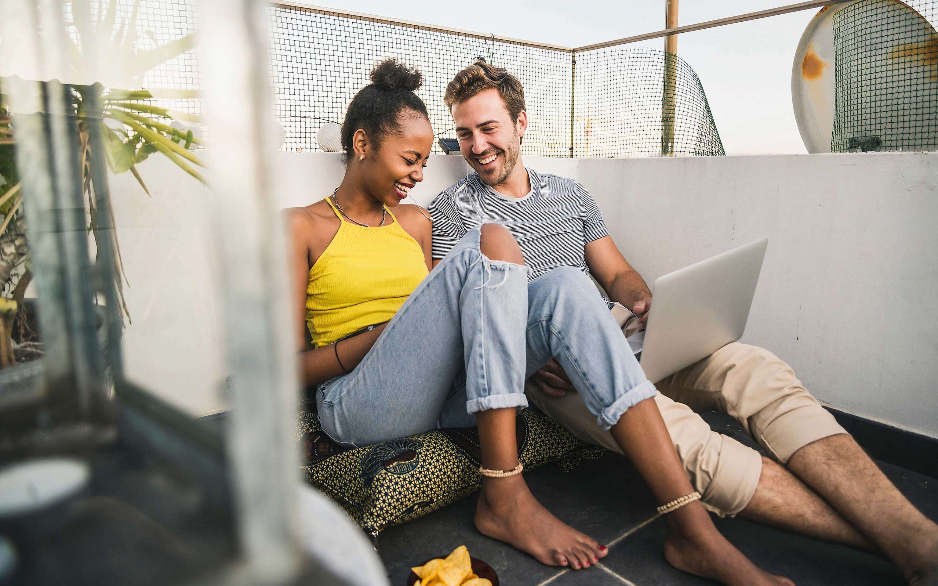 So fühlt sich gute Energie mit Yello an Junges, fröhliches Paar mit Laptop sitzt auf dem Balkon