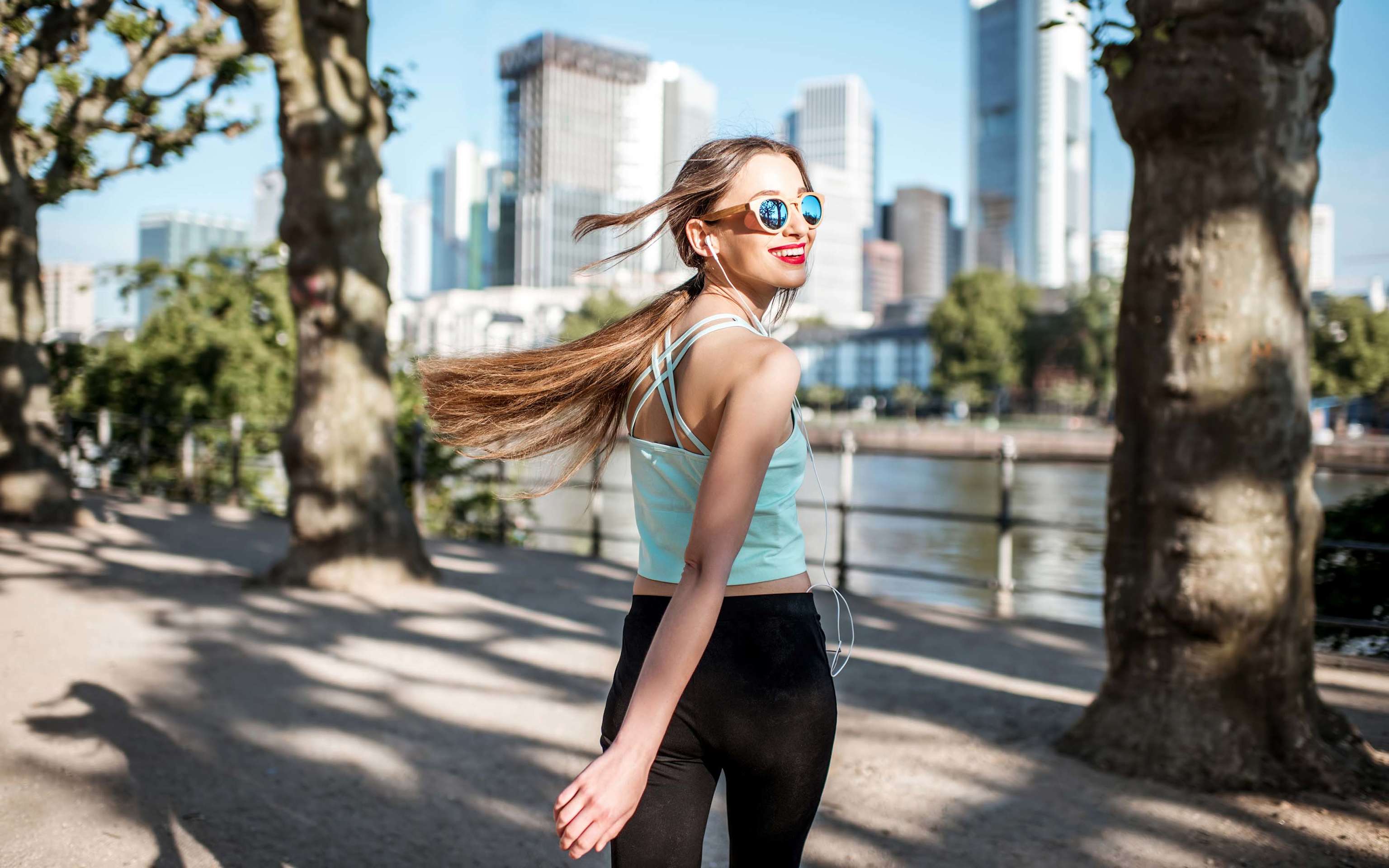 Eine junge Frau in Sportbekleidung geht und blickt zurück im Park mit Wolkenkratzern im Hintergrund in Frankfurt Eine junge Frau in Sportbekleidung geht und blickt zurück im Park mit Wolkenkratzern im Hintergrund in Frankfurt