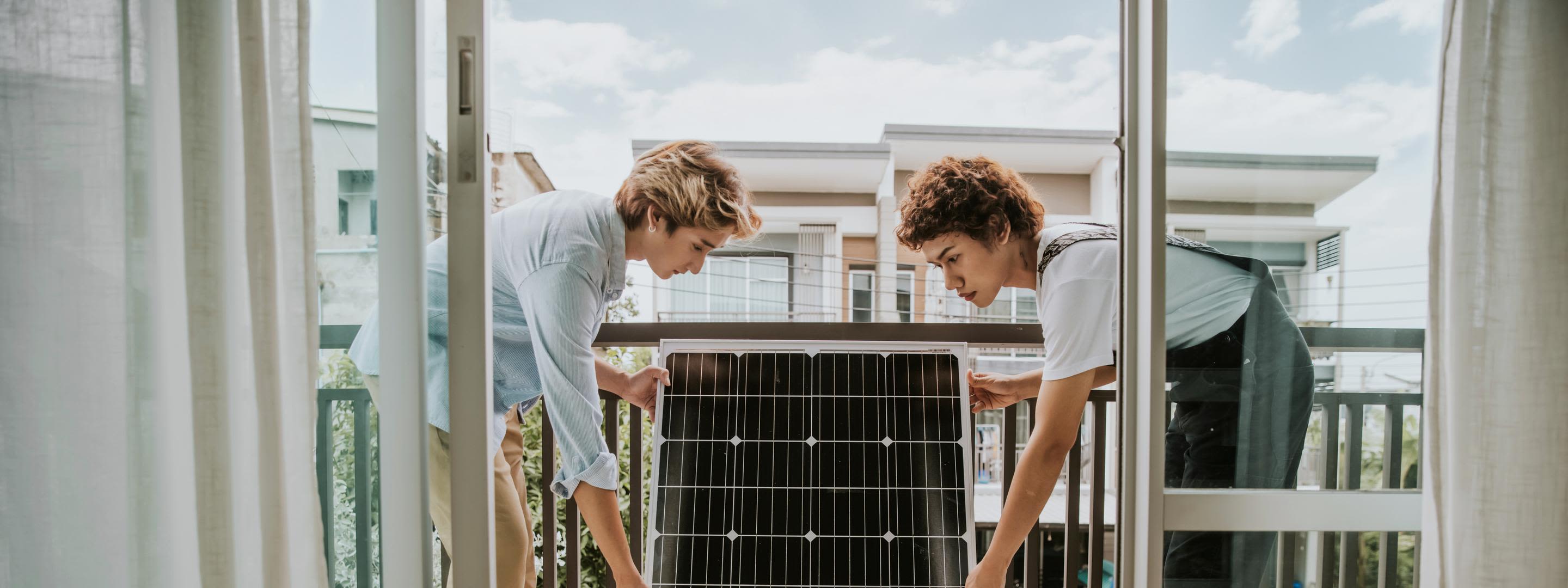 Mit Balkonsolar zuhause grün unterwegs Zwei junge Frauen installieren ein Solarmodul auf dem Balkon