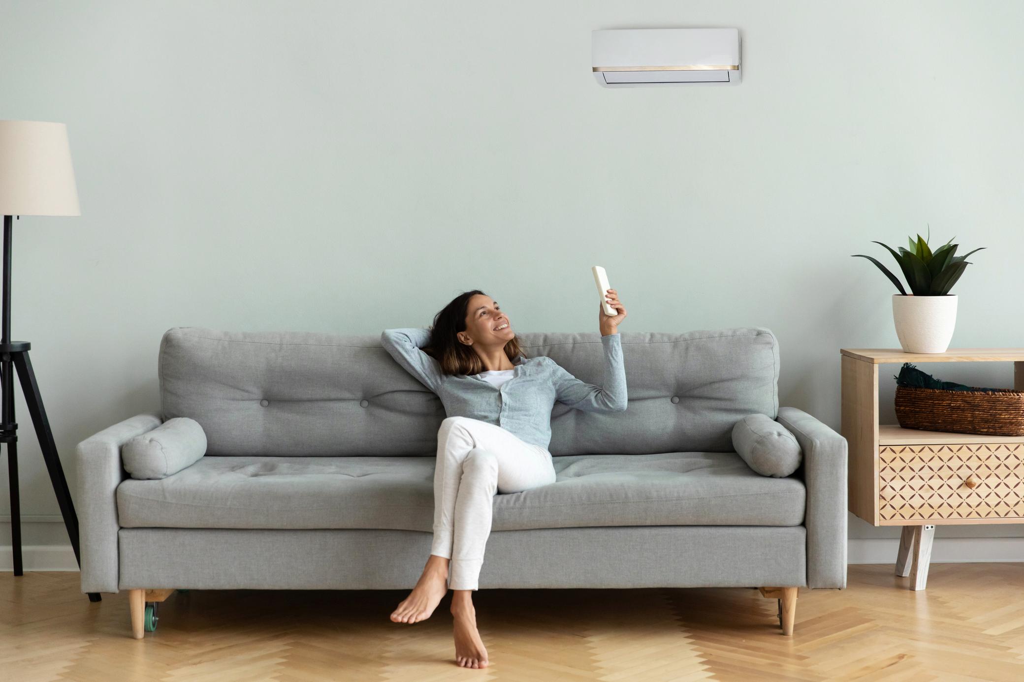 Frau sitzt auf der Couch un bedient eine Klimaanlage