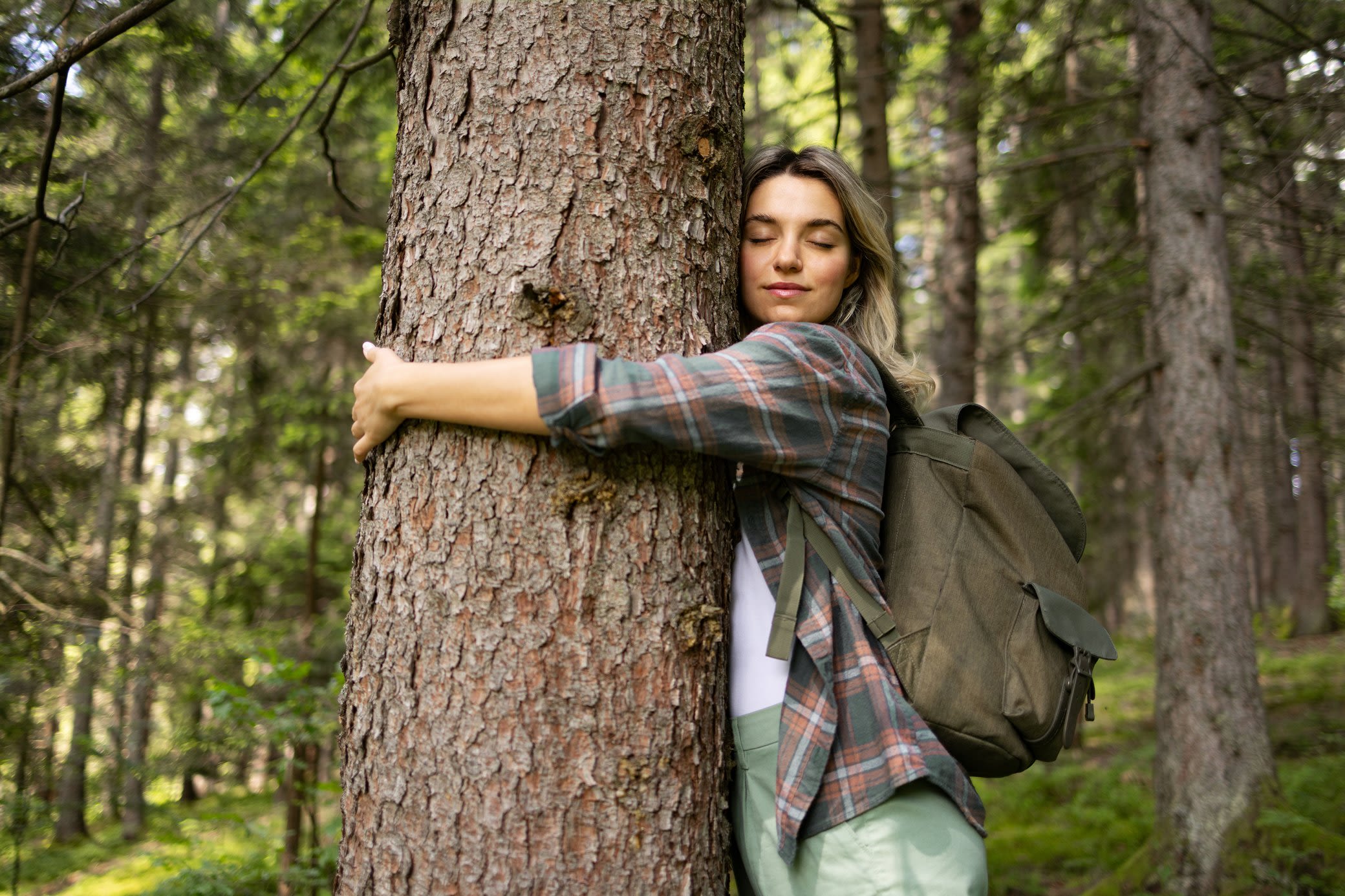 Natur- und Klimaschutz sind uns bei Yello ein Anliegen Frau umarmt mit geschlossenen Augen einen Baum in einem Wald