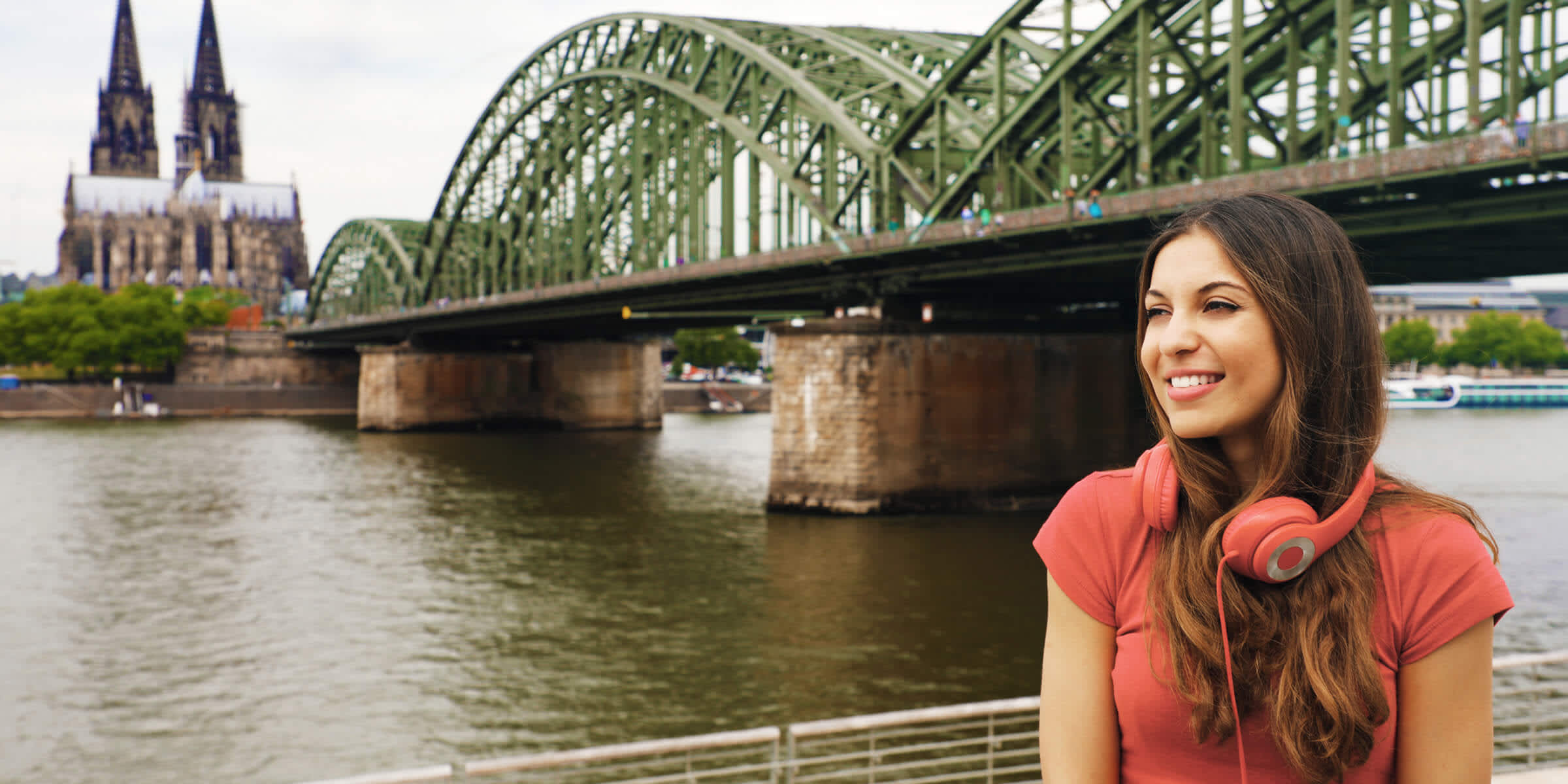 Frau mit Kopfhörern sitzt vor der Hohenzollerbrücke am Rhein in Köln Frau mit Kopfhörern sitzt vor der Hohenzollerbrücke am Rhein in Köln