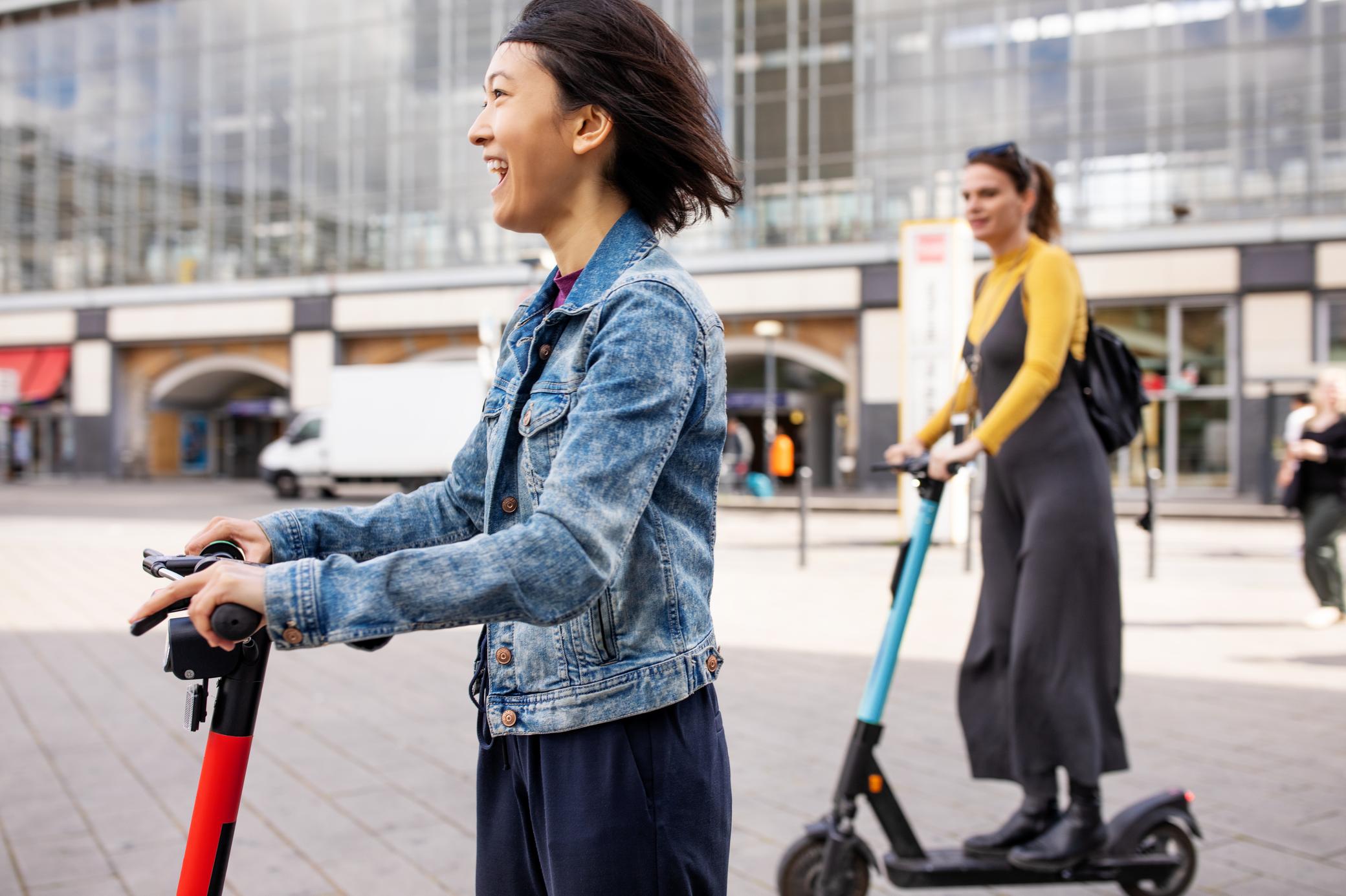 Zwei junge Frauen fahren mit dem E-Scooter in der Stadt