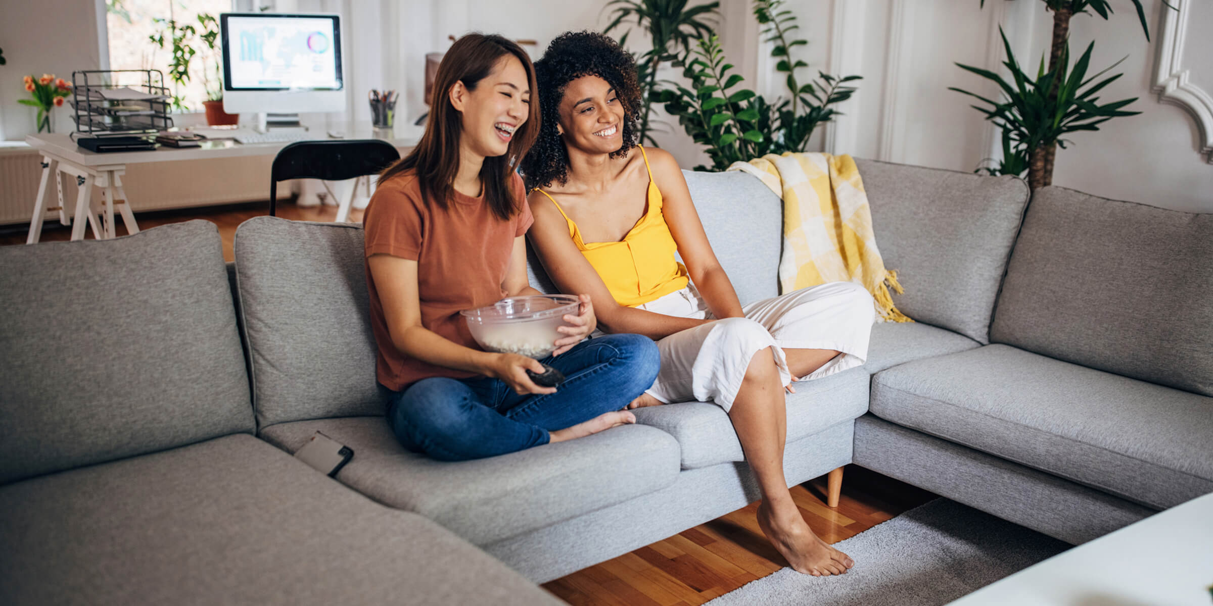 Zwei Frauen sitzen mit Popcorn vor dem Fernseher.