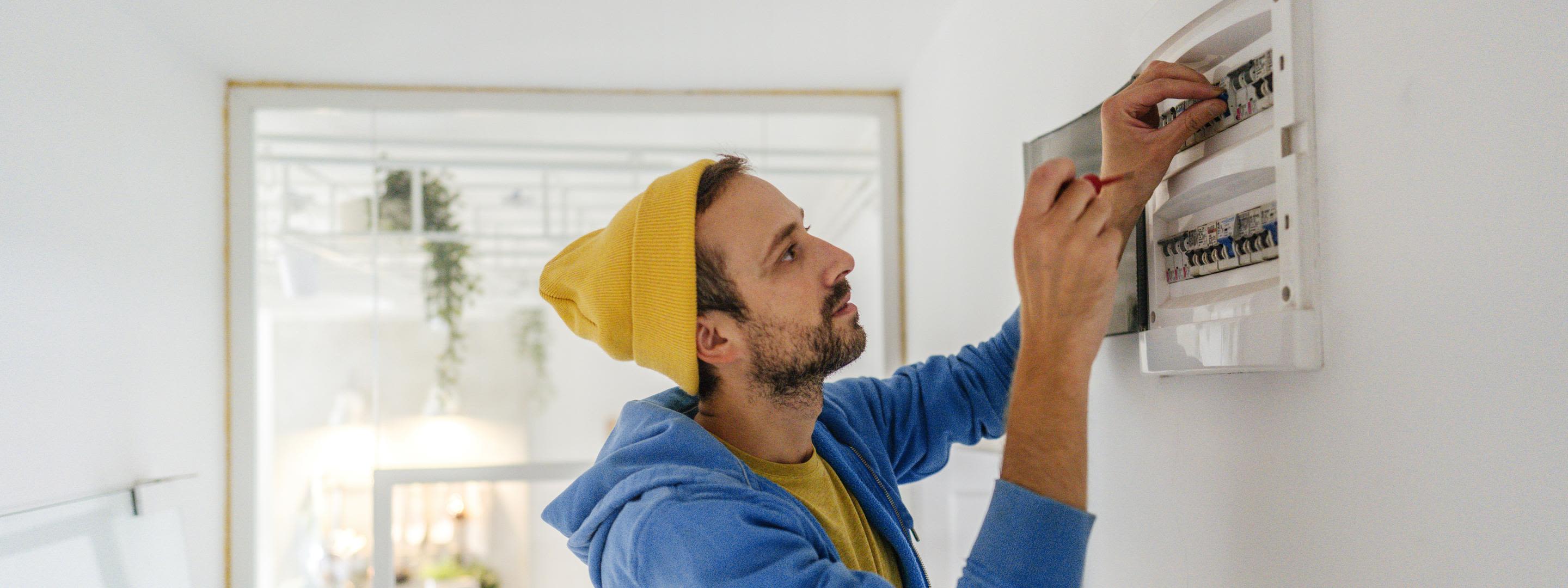 Strombegriffe einfach verstehen: Von Stromlieferant bis Netzbetreiber Junger Elektriker arbeitet an einen Sicherungskasten