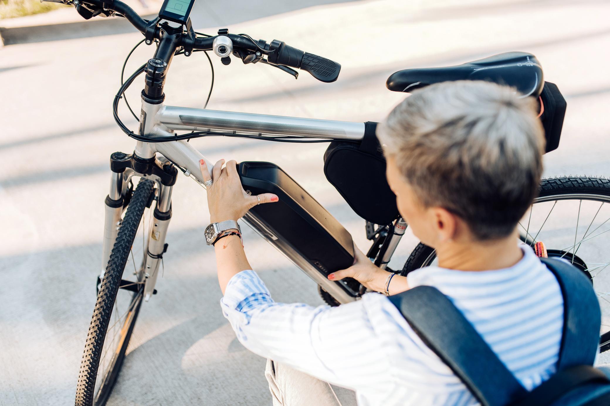 Frau wechselt die Batterie ihres E-Bike