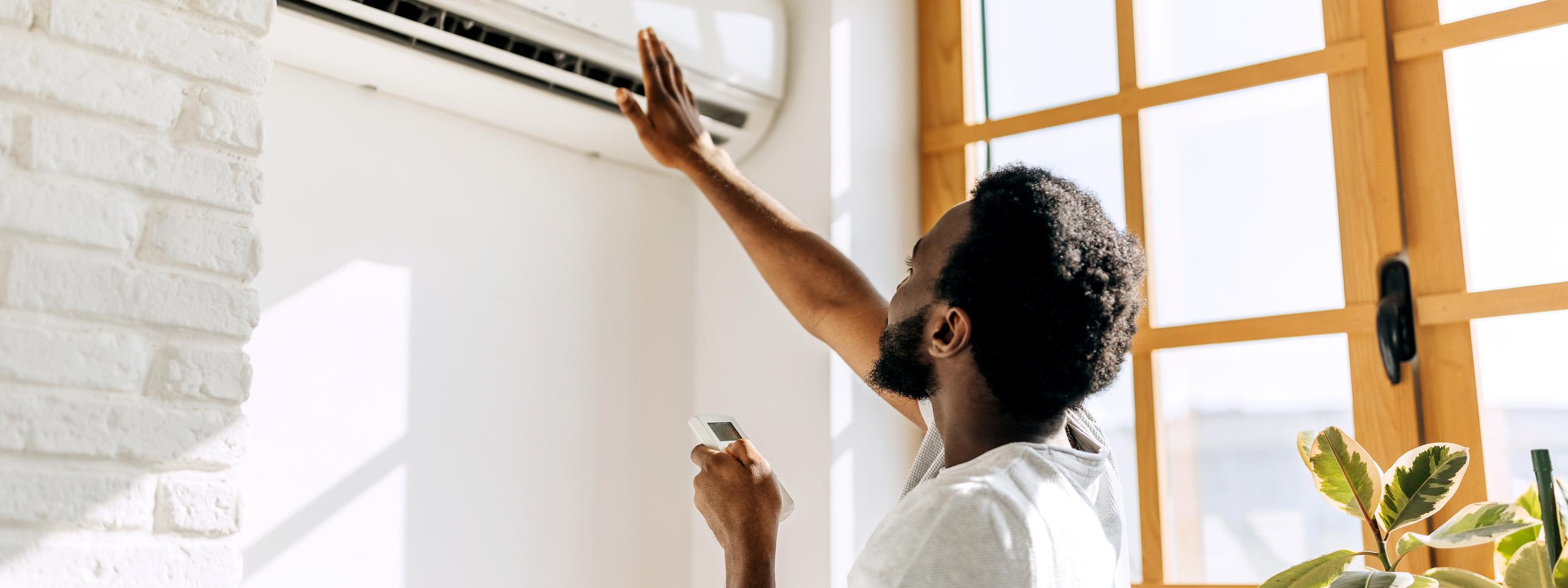 Mit einer Klimaanlage Zuhause durch den heißen Sommer Mann in weißem T-Shirt und Fernbedienung prüft den Luftzug seiner Klimaanlage