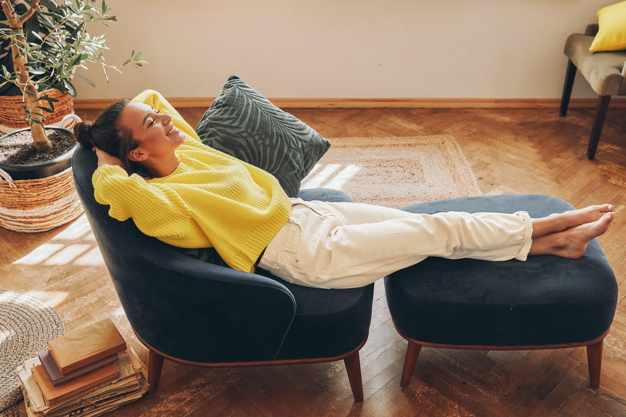 Zuhause gute Energie einziehen lassen und entspannt zurücklehnen Eine Frau im gelben Pullover lehnt sich entspannt im Wohnzimmersessel zurück
