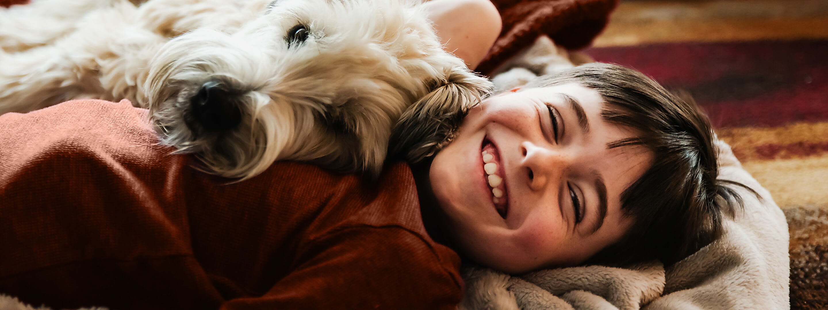 Mit Wärmepumpe kannst du zuhause nachhaltig heizen. Ein Junge kuschelt mit einem Hund auf dem Boden