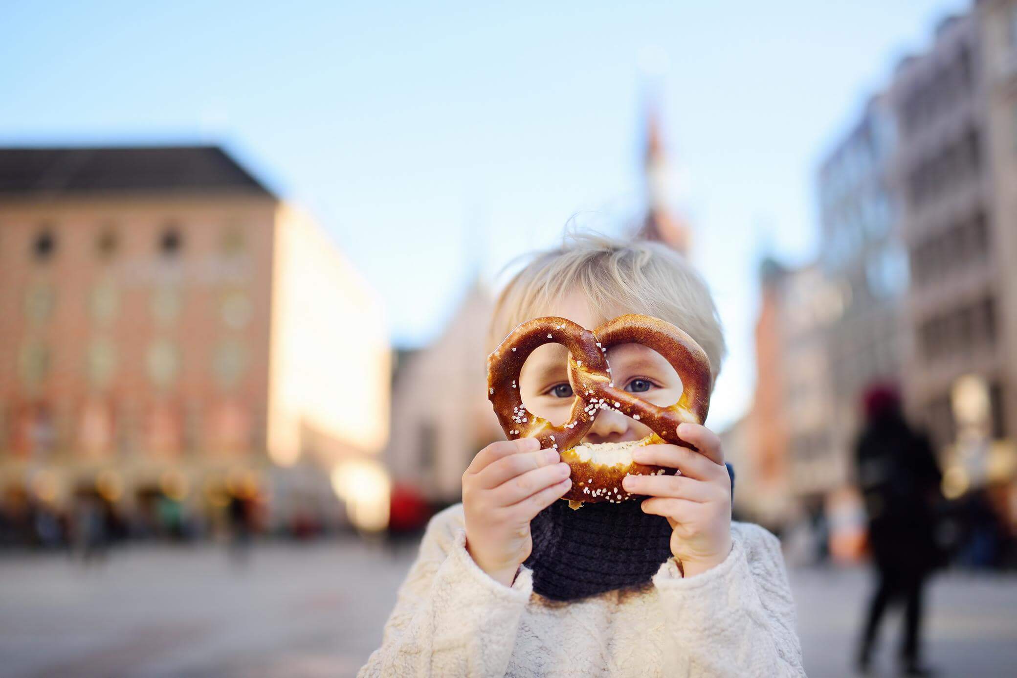 Ein kleiner Junge hält sich eine Brezel vor sein Gesicht.