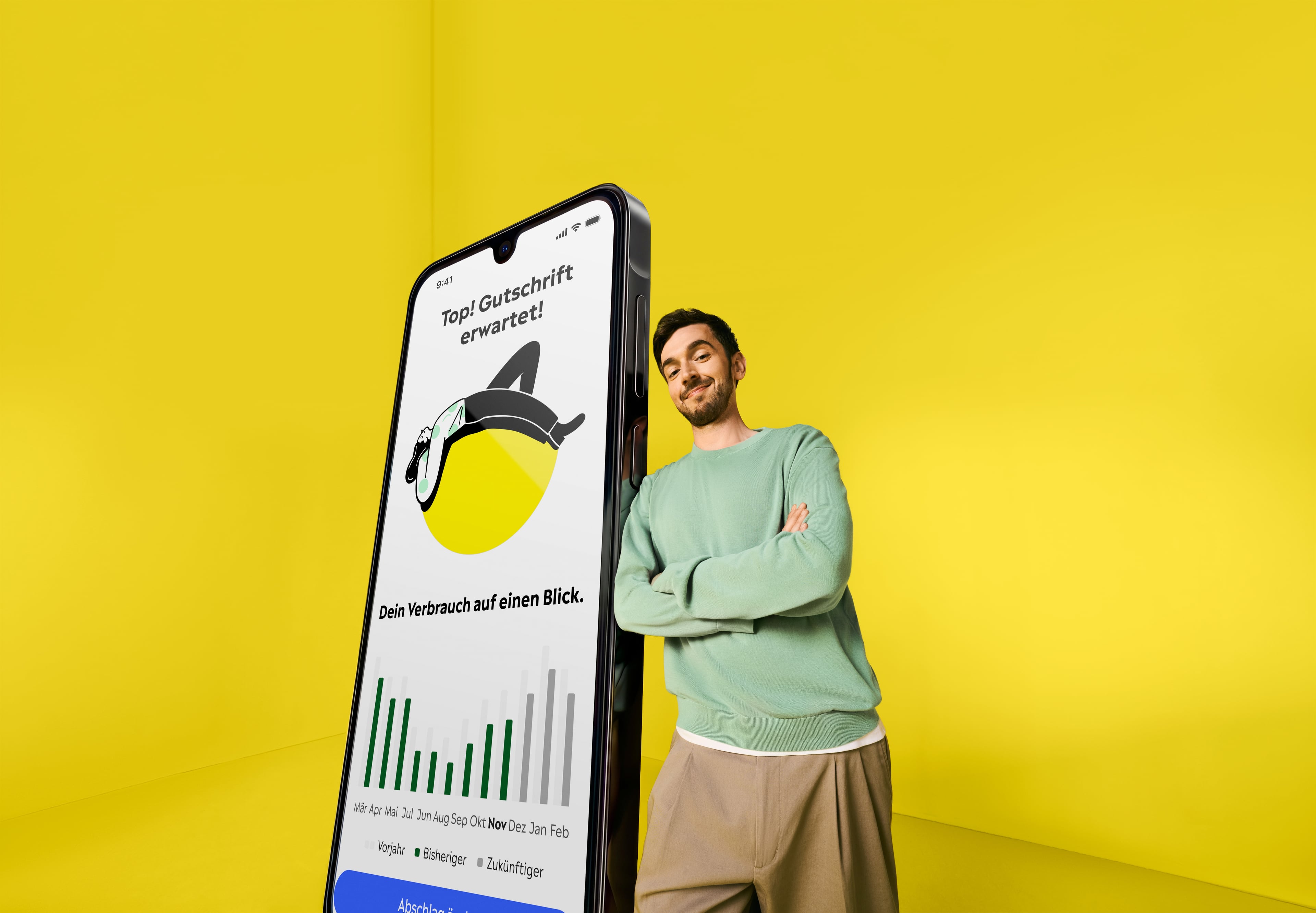 Yello Mann steht in einem gelben Raum und lehnt sich an ein übergroßes Smartphone, auf dem die Yello App zu sehen ist.