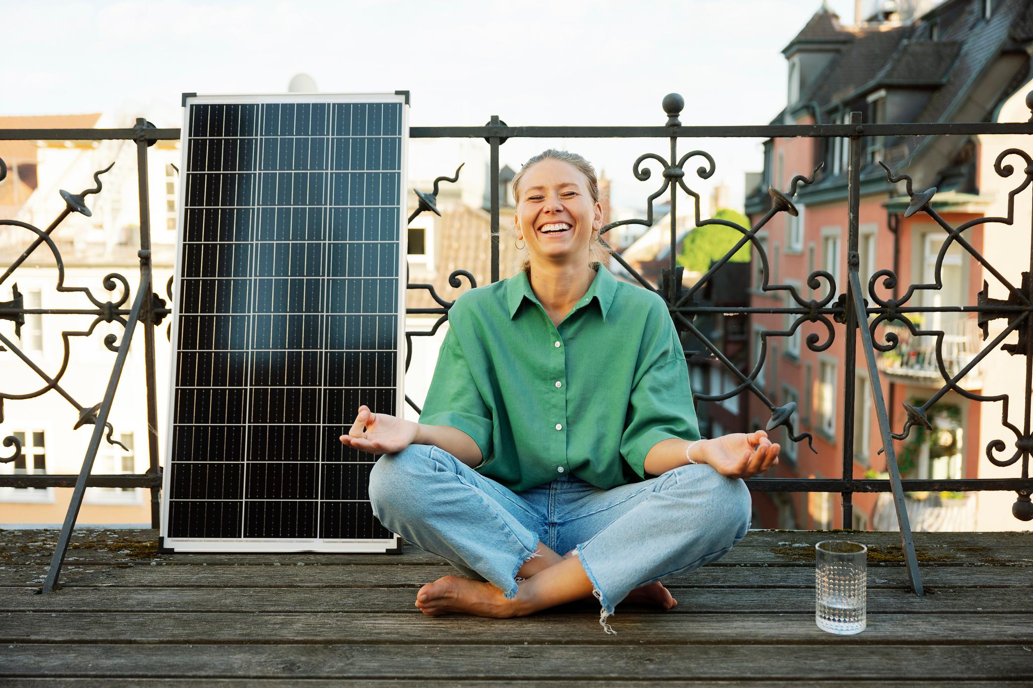 Frau macht Yoga auf dem Balkon. Neben ihr ist ein Solarpanel.