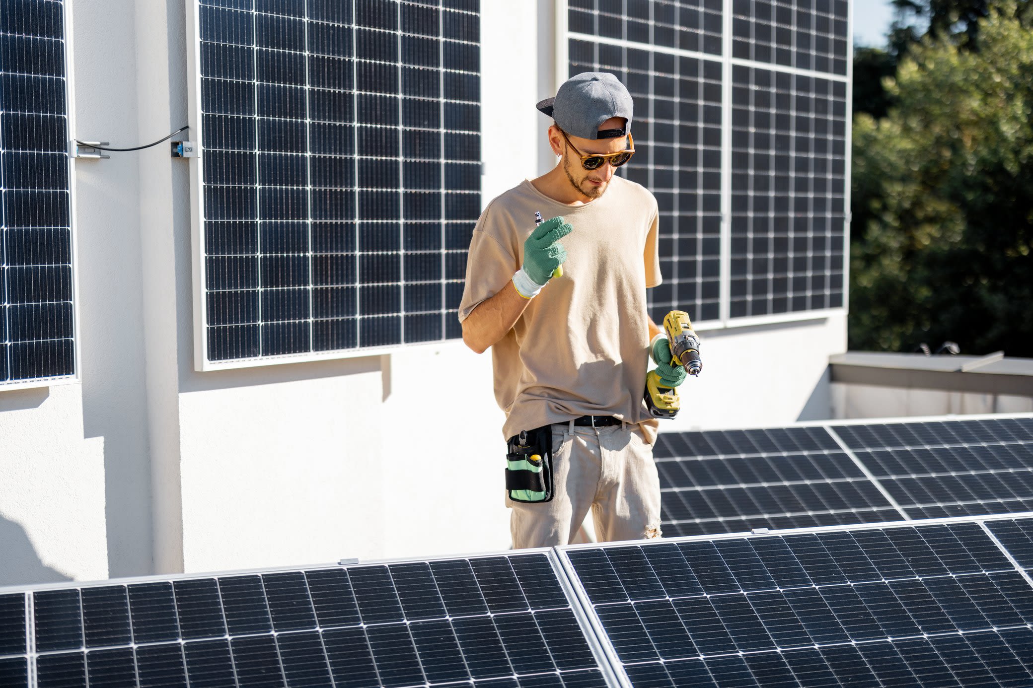 Auf einen Blick: Was alles zu einem Komplettpaket für Solar dazugehört. Mann mit Sonnenbrille und Kappe befestigt mit Akkuschrauber Solarmodule auf Balkon.