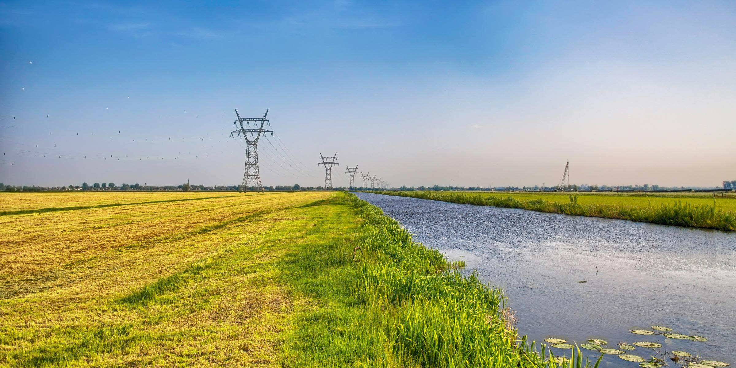 Für den Transport von Strom zahlen wir Netzentgelte Hochspannungsleitungen und Strommasten auf einem Feld an einem Kanal