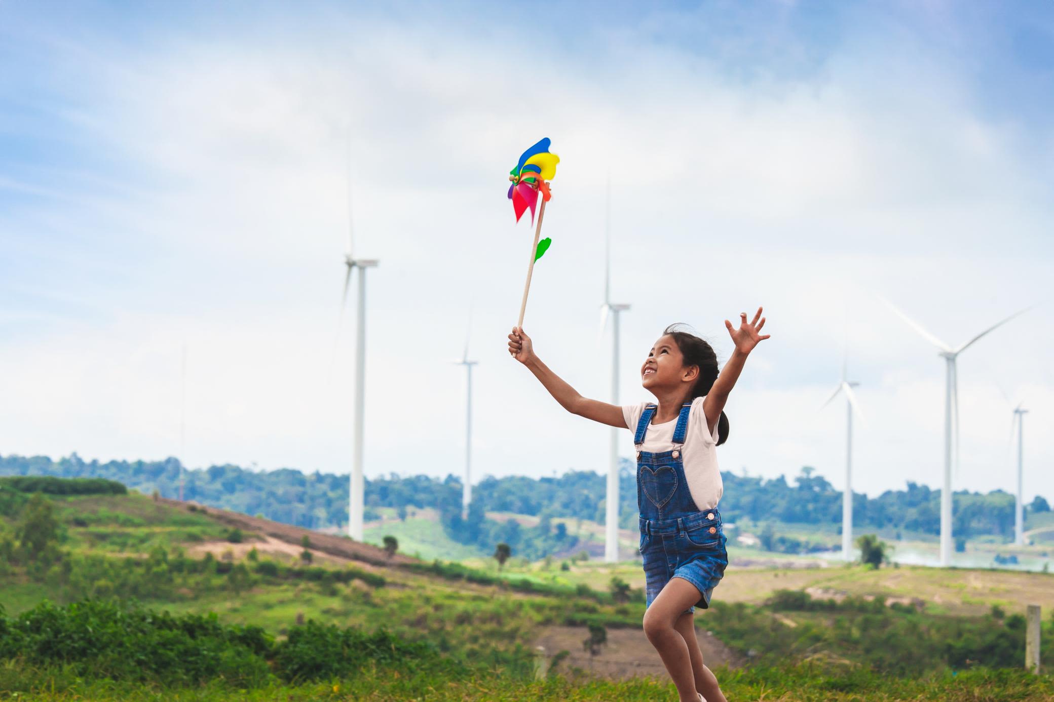 Mehr als erneuerbare Energie: Mit Windenergie zu unabhängiger Energieversorgung Mädchen läuft mit buntem Windrad durch einen Windpark