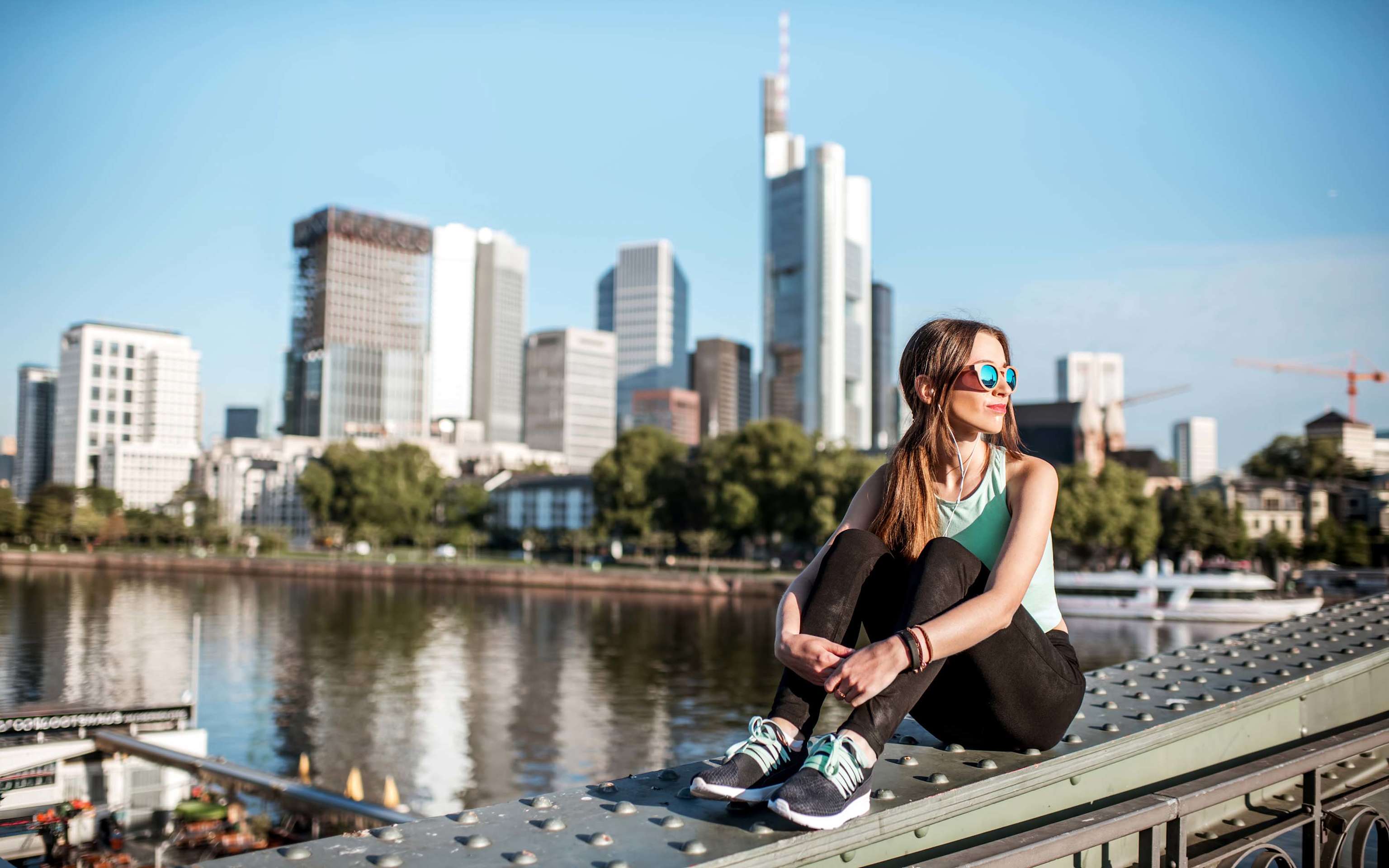 Junge Frau sitzt auf der Brücke mit tollem Blick auf die moderne Stadt Frankfurt Junge Frau sitzt auf der Brücke mit tollem Blick auf die Stadt Frankfurt