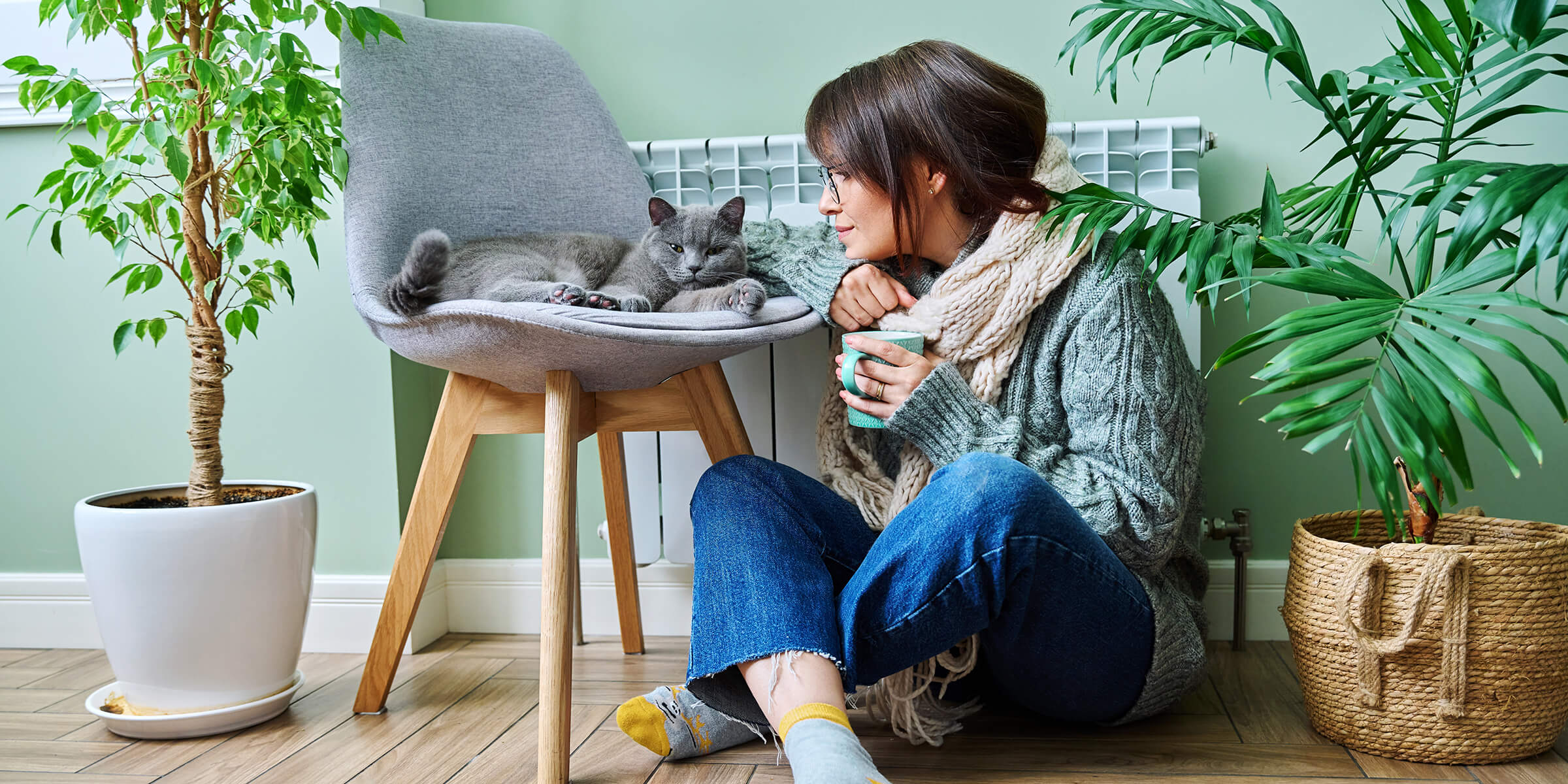 Frau sitzt in warmer Kleidung mit Katze vor der Heizung.