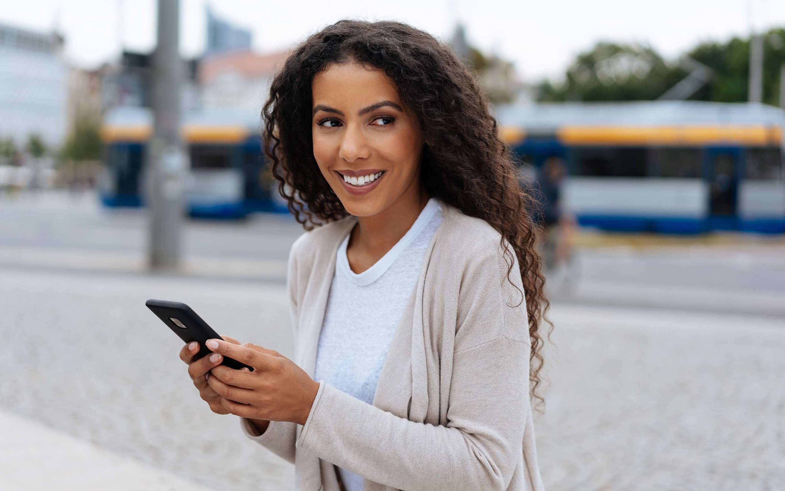 Lachende Frau vor der Leipziger U-Bahn mit Blick auf ihr Smartphone. Lachende Frau vor der Leipziger U-Bahn mit Blick auf ihr Smartphone