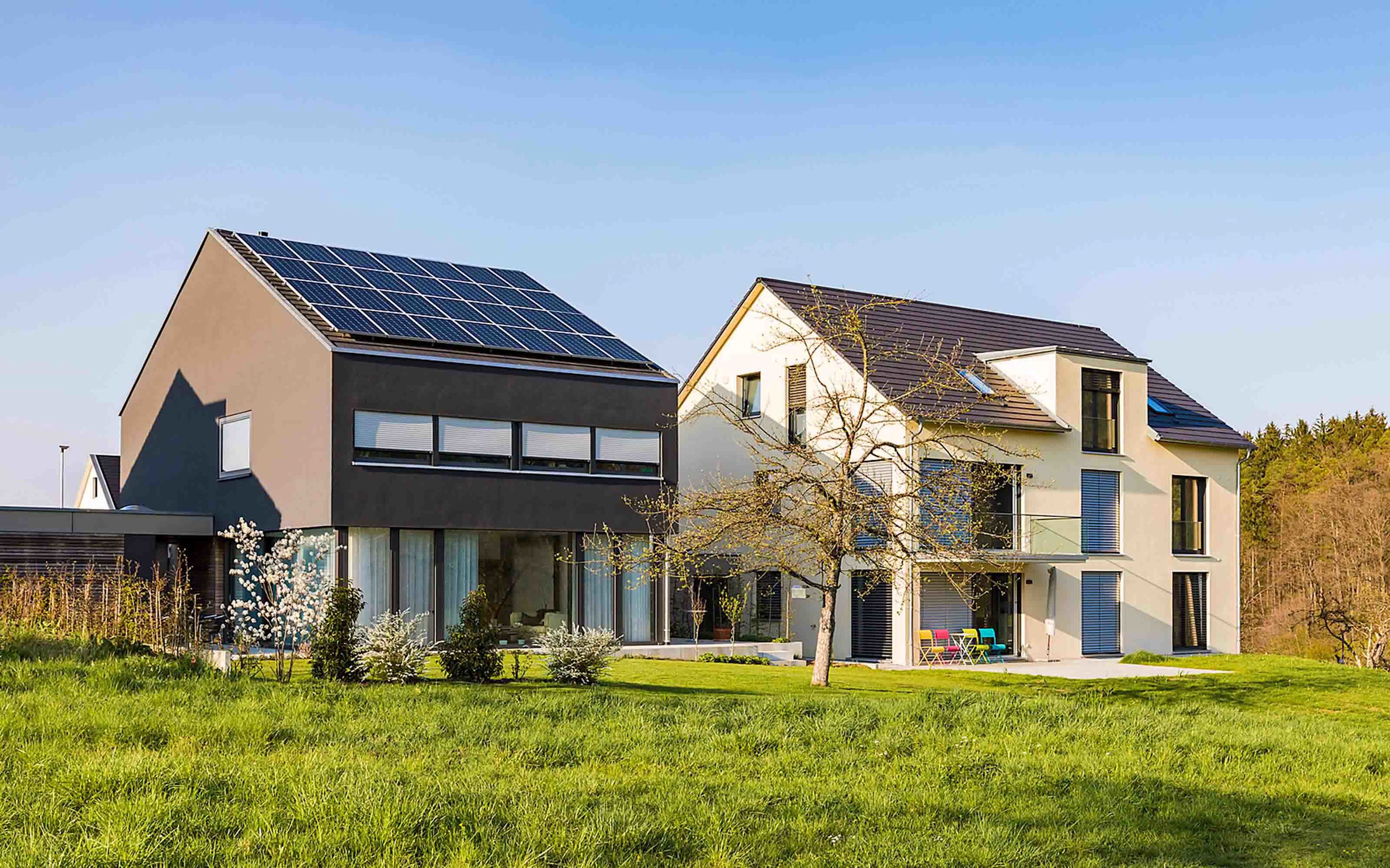 Solarstrom lokal mit Nachbarn teilen – neu über Energy Sharing Modernes Einfamilienhaus mit Photovoltaik-Anlage steht neben Haus ohne Photovoltaik-Anlage