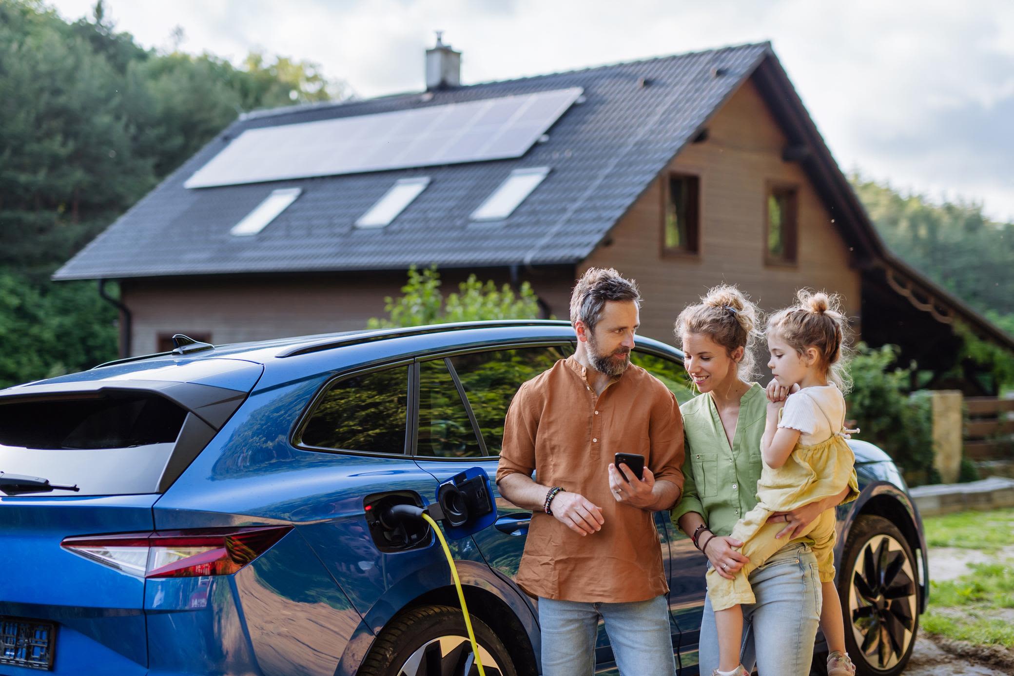 Ob Volleinspeisung oder Eigenbedarf - mit Solar auf dem Dach hat man viele Vorteile und Möglichkeiten. Familie mit Mädchen laden Elektroauto vor dem Haus mit Solaranlage auf dem Dach