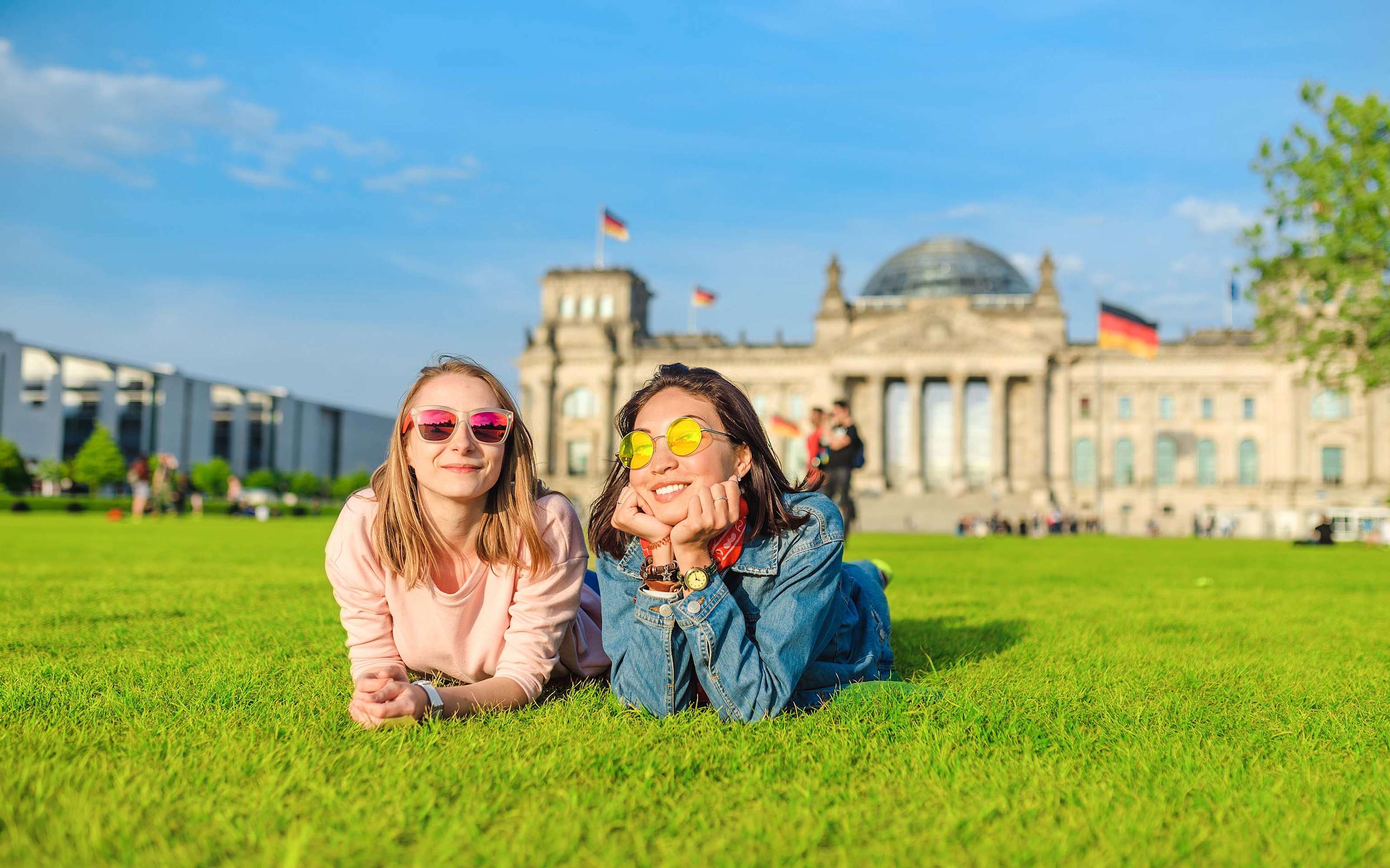 Als dein fairer Gasanbieter sorgen wir für gute Energie in Berlin Zwei Frauen liegen vor dem Reichstagsgebäude in Berlin auf der Wiese