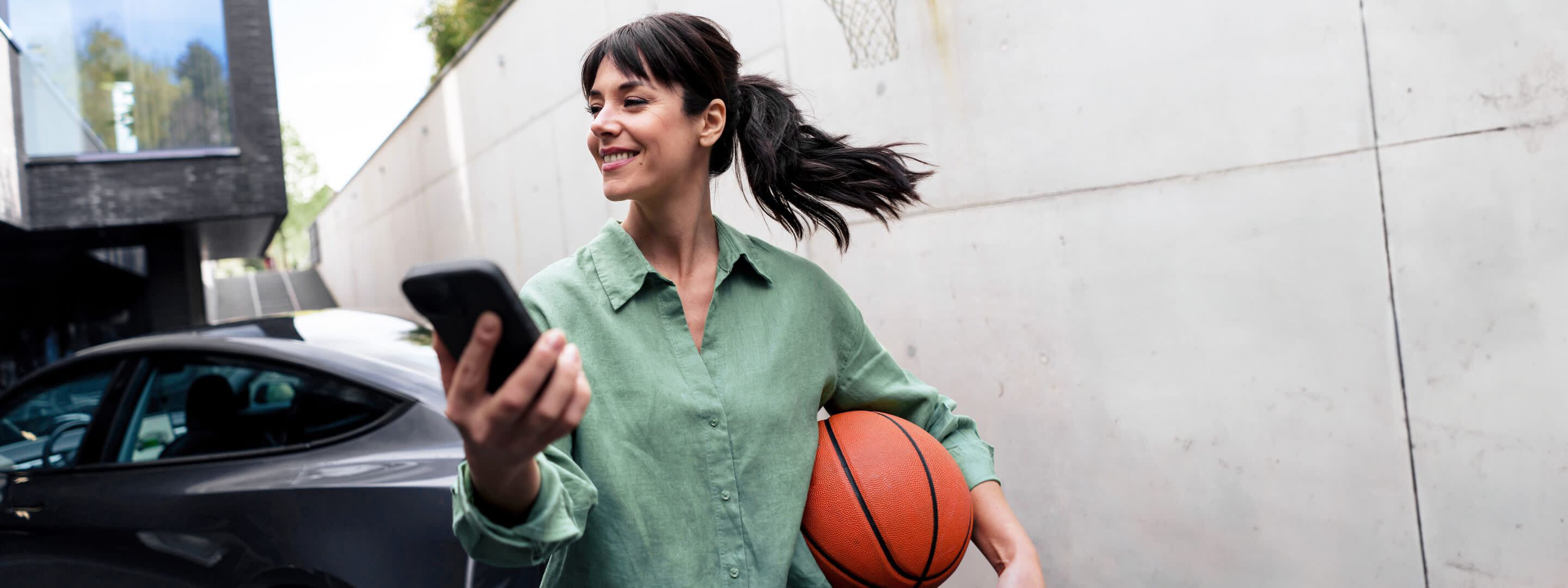 So funktionieren flexible Stromtarife - von dynamisch bis variabel Frau mit Basketball und Handy lädt ihr E-Auto zuhause