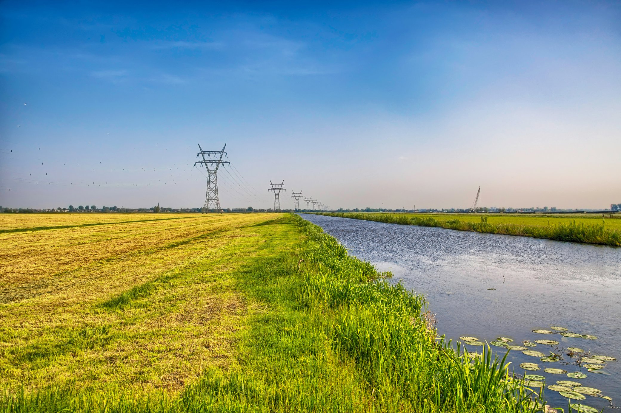 Hochspannungsleitungen und Strommasten auf einem Feld an einem Kanal