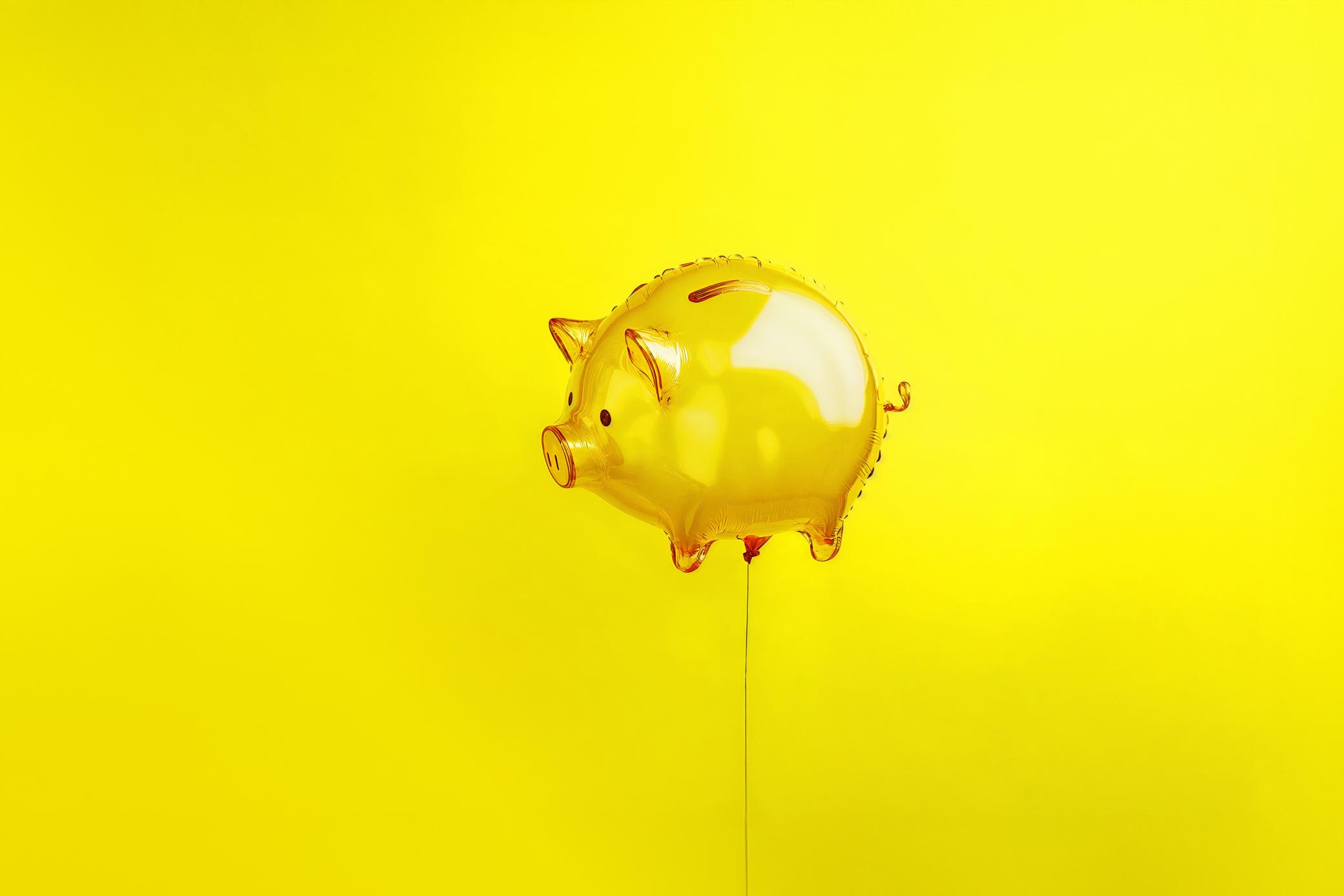 Ein gelbes Sparschwein in Luftballon Form schwebt vor gelbem Hintergrund. 
